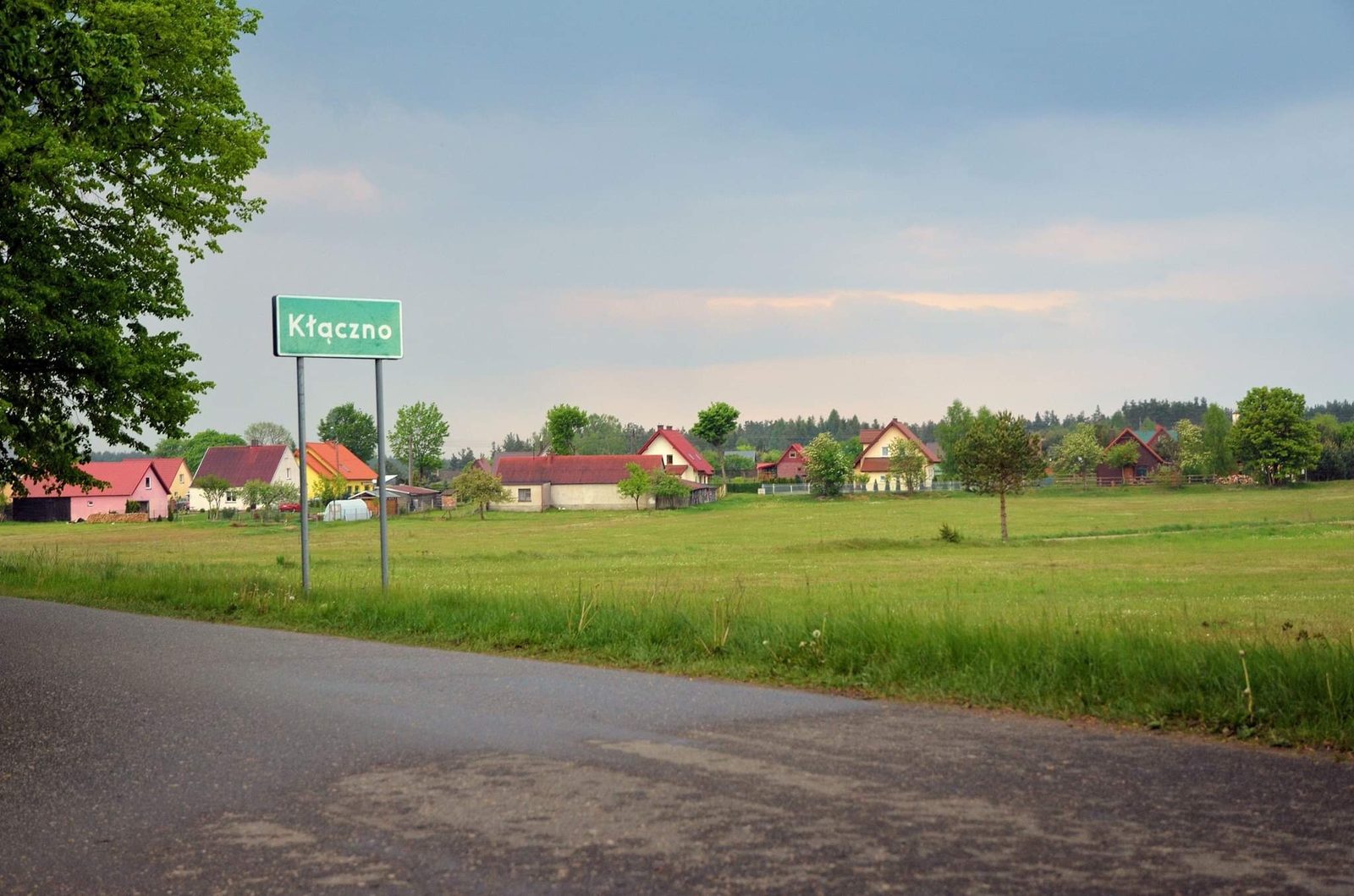 Tablica z nazwą wsi Kłączno i zabudowania w tle
