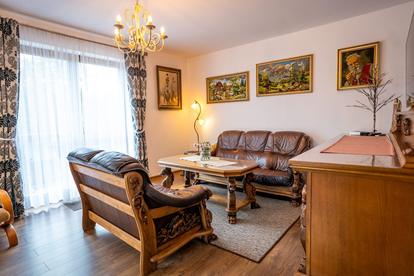 Salon domu Słonecznik w dziennym świetle, skórzana sofa i żyrandol